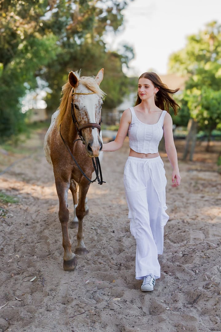Woman and Appaloosa walking down a sand track.